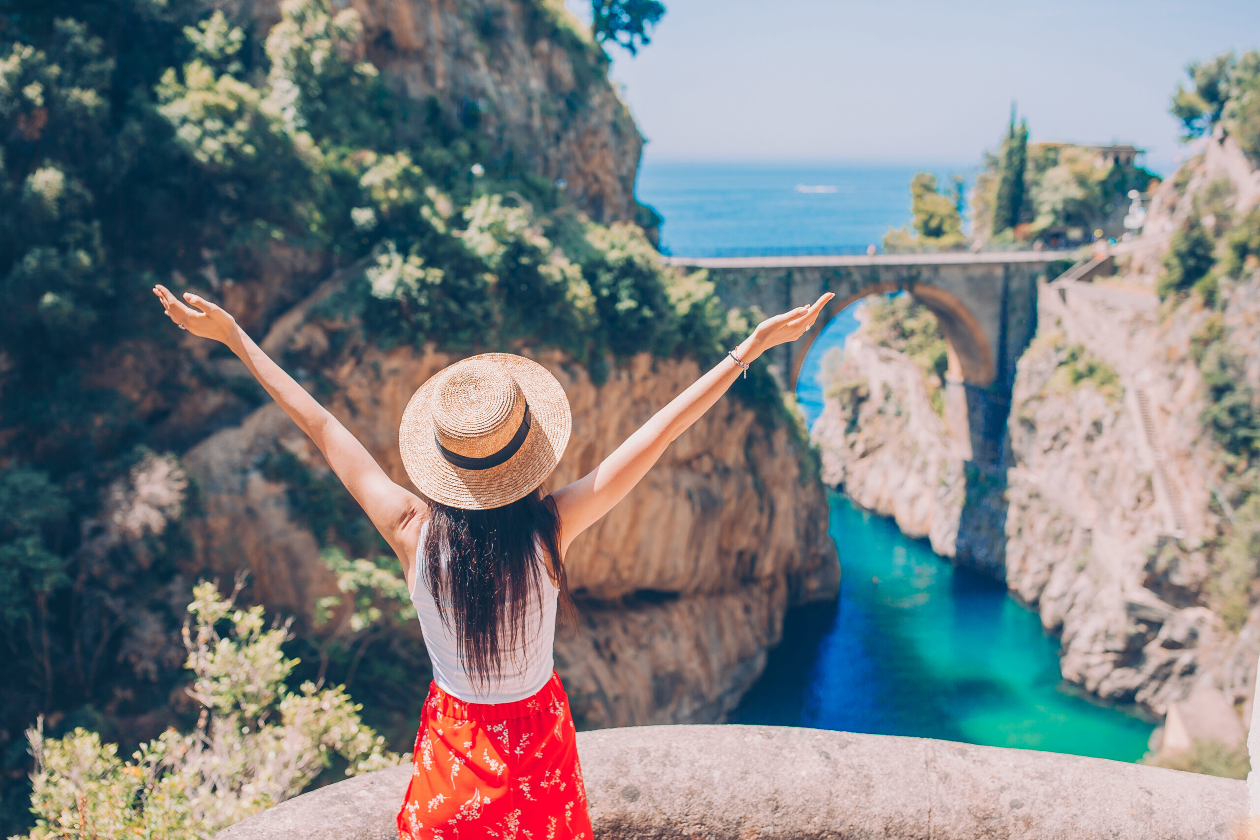 Back view of beautiful woman enjoy the amazing view of Fiordo di Furore. Cala di Furore beach, bridge over the gorge Fiordo di Furore.