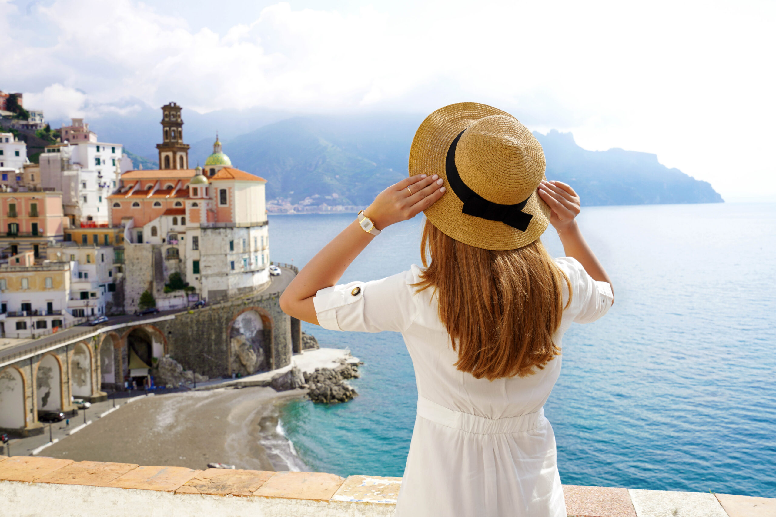 Tourism in Italy. Back view of girl holding hat looking Atrani village on Amalfi Coast, Italy.