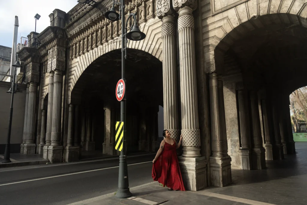 Woman in a flowing red dress posing under the ornate arches and columns of Çırağan Bridge in Istanbul, Turkey.