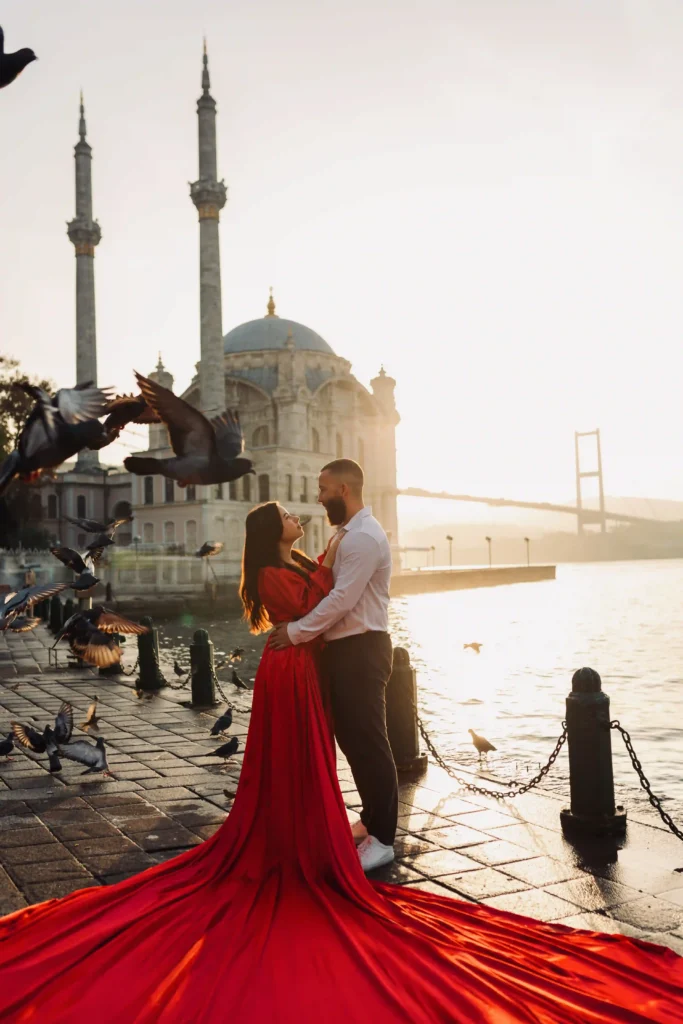 Couple hugging at sunrise by Ortaköy Mosque and the Bosphorus Bridge in Istanbul, with pigeons red flying dress