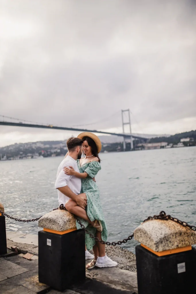 Couple embracing by the Bosphorus in Ortaköy with the Bosphorus Bridge in the background on a cloudy day.
