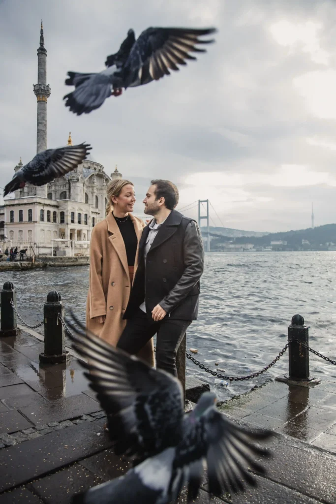 Couple by the Bosphorus near Ortaköy Mosque with pigeons in flight and the bridge behind.