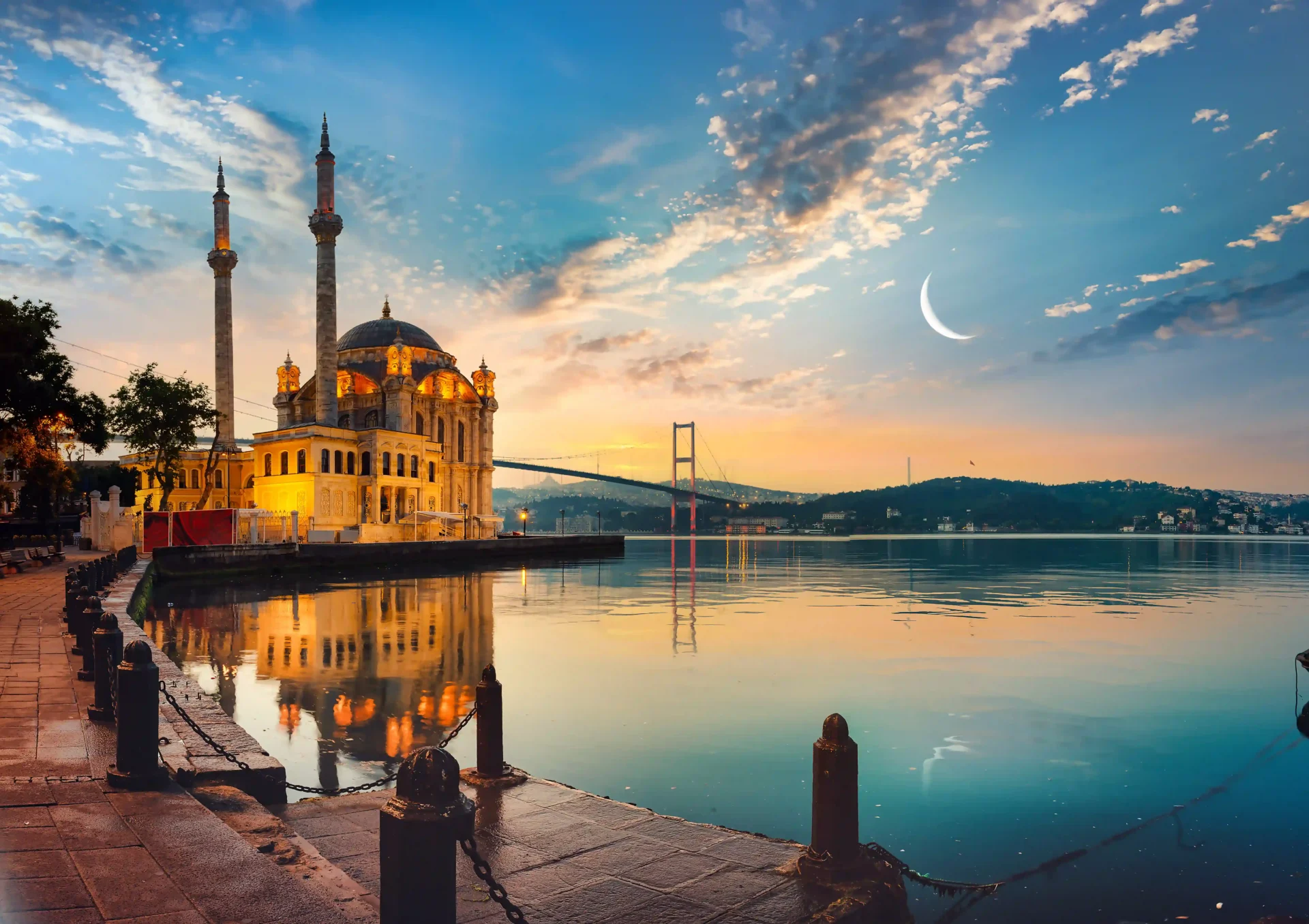 Ortaköy Mosque illuminated at blue hour beside the Bosphorus, reflecting on calm water with the Bosphorus Bridge in the background.